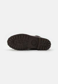 Suela de zapato de goma negra con un patrón de banda de rodadura robusto, que presenta surcos profundos y pequeños salientes para tracción y estabilidad. Logo circular en el centro.