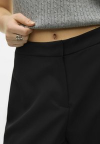 Svarte høy midje bukser med en glatt tekstur, med en skjult sidelommer, båret med en kort grå ribbestrikket genser.