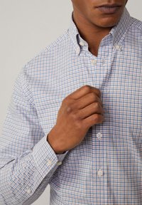 Overhemd met knoopsluiting van een lichte stof met een blauw en roze geruit patroon, een puntige kraag en parelachtige knopen.