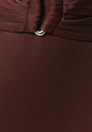 Gros plan sur un tissu marron avec des fronces cousues et un petit anneau décoratif argenté au centre.