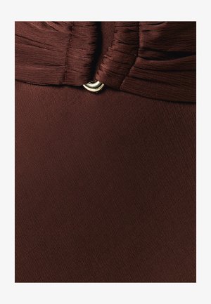 Gros plan sur un tissu marron avec des fronces cousues et un petit anneau décoratif argenté au centre.