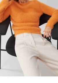 Oranje fuzzy trui met een ronde halslijn, gecombineerd met crèmekleurige geplooide broeken. De outfit heeft zachte texturen en een relaxed pasvorm.