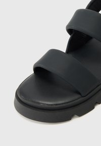 Mustad mustad, millel on kaks laia rihma, lame tald ja tekstureeritud pind rihmadel; moodne disain koos tugeva kummitaldaga.
