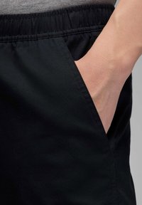 Črne kratke hlače z elastičnim pasom in stranskimi žepi, gladke mat teksture z minimalnimi šivi.