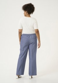 Pantaloni a gamba larga in tessuto azzurro chiaro con finitura testurizzata e vita elastica, abbinati a una maglietta aderente bianca. Design minimalista.