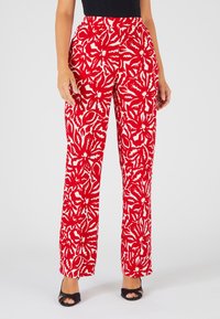 Rode bloemenpatroon broek met opvallende witte bladsneden. Hoge taille, recht gesneden, gemaakt van een textuurstof, gedragen met zwarte hakken.