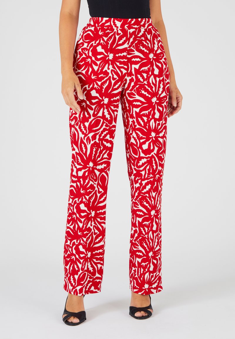 Rode bloemenpatroon broek met opvallende witte bladsneden. Hoge taille, recht gesneden, gemaakt van een textuurstof, gedragen met zwarte hakken.