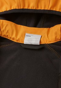 Veste en polaire noire avec un intérieur présentant une doublure de capuche orange, des coutures contrastées et une étiquette portant l'inscription « J'étais ici ».