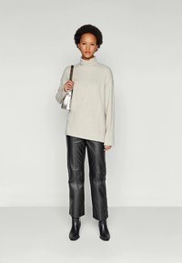 Light beige turtleneck sweater, loose fit; black faux leather pants with side stitching; black ankle boots; small metallic shoulder bag.