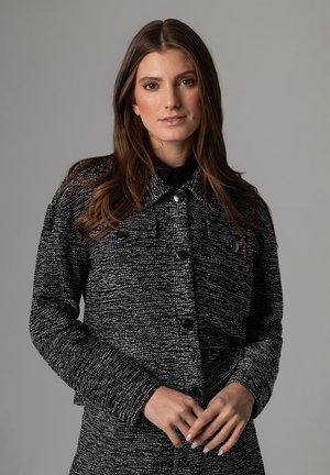 Black and white textured jacket with a collar, front buttons, and two chest pockets. Long sleeves and a fitted silhouette.