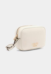 Vaaleanbeige suorakaidehandbag, jossa on vetoketjusuljenta, kultaiset yksityiskohdat ja kohokuvioitu brändilogo. Varustettu irrotettavalla hihnalla, jossa on vastakkaiset korostukset.