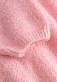 Zachte, pluizige roze gebreide stof met duidelijk zichtbare geribbelde boorddetails, die textuur en zachte plooien toont.