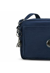 Borsa a tracolla blu navy testurizzata con tasca frontale, portachiavi a forma di scimmia argentata e emblemma rotondo sul fronte.