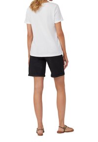 T-shirt en coton blanc, manches courtes, coupe décontractée, associé à un short en denim noir, ourlets retroussés, et des sandales marron avec un accent en imprimé léopard.