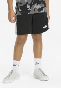 Pantaloni sportivi neri con tasche laterali, pannelli laterali grigi e logo PUMA. Abbinati a calzini bianchi e scarpe sportive grigio chiaro.