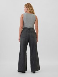 Un jean large gris foncé avec une taille haute, des poches arrière et des coutures contrastées. Associé à un débardeur gris ajusté.