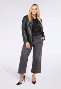 Svart faux läderjacka med en figursydd silhuett, med dragkedjefickor, bärs över en texturerad svart topp och kombineras med högmidjade grå vida jeans och svarta klackar.