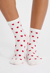 Calzini bianchi in cotone con un motivo di piccoli cuori rossi, progettati con un bordo a costine e una superficie liscia.