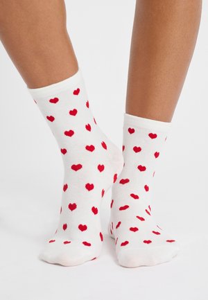 Weiße Baumwollsocken mit einem Muster aus kleinen roten Herzen, gestaltet mit einem gerippten Bund und einer glatten Textur.