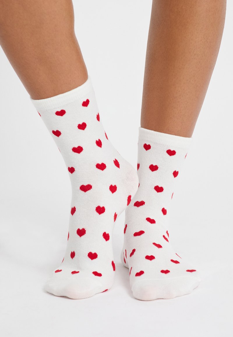Calzini bianchi in cotone con un motivo di piccoli cuori rossi, progettati con un bordo a costine e una superficie liscia.