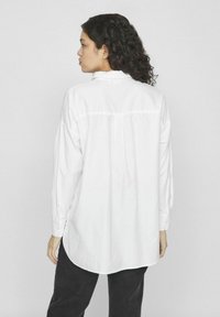 Camisa blanca de manga larga con corte relajado, con dobladillo curvado, puños abotonados y detalle en la Y en la parte posterior. Tejido texturizado.