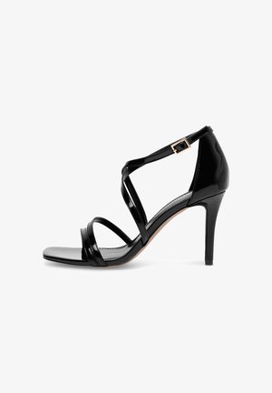 Sandalo con tacco alto in pelle verniciata nera con sottili cinturini che attraversano il piede e una piccola fibbia intorno alla caviglia.