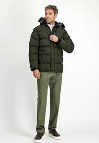 Donkergroene gewatteerde jas met een capuchon, voorzien van een nep-bont accent. Gekozen over een witte trui, gecombineerd met olijfgroene broeken en donkere schoenen.