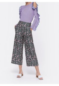 Lavendelribbat stickat topp med volangärmar, tillsammans med vida byxor med grönt blommönster. Vita slidesandaler fulländar outfiten.