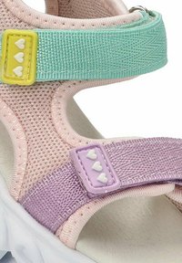 Sandalia multicolor que presenta materiales de malla y tela en rosa, verde y púrpura. Incluye adornos decorativos en forma de corazón en las correas.