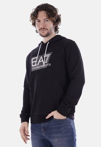 Felpa nera con cappuccio e design del logo sul petto, con tasca a marsupio e lacci bianchi. Tessuto morbido con vestibilità casual.
