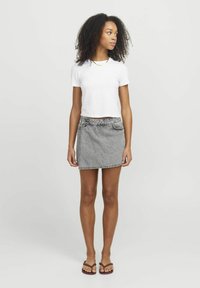 Gonna di jeans grigia con vita alta, orlo sfilacciato e tasca laterale. Abbinata a una maglietta bianca attillata e ciabatte marroni.