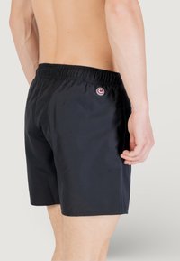 Costume da bagno neri realizzati in tessuto leggero, dotati di un elastico in vita e un piccolo logo circolare sul lato sinistro posteriore.