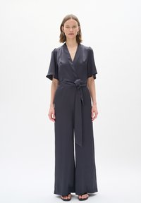 Tuta grigia con design avvolgente, maniche corte, cintura legata in vita e pantaloni a gamba larga, realizzata in un tessuto liscio e morbido.