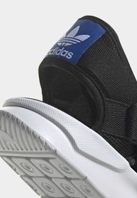 Black Adidas sneaker heel with blue logo patch and white textured sole, showing detailed fabric and stitching.
