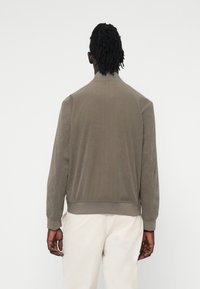 Olive roheline bomber-jakk pehmest kangast, ribitud mansettide jaäärtega. Omab siledat tekstuuri ja minimalistlikku disaini, tagapoolt vaade.