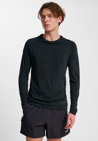 Zwarte sportshirt met lange mouwen van rekbare stof, met een textuurlogo en naadloos ontwerp, gecombineerd met zwarte shorts.