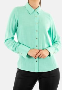 Camicia a maniche lunghe verde menta chiaro con colletto a punta, dotata di bottoni dorati sulla parte anteriore e dettagli con bottoni sui polsini.