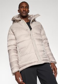 Jachetă puffer de culoare bej deschis, cu design matlasat orizontal, fermoar frontal, nasturi cu capsa și glugă. Materialul pare neted și ușor lucios.