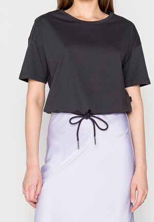 Black cropped t-shirt made of soft material, featuring a round neckline and short sleeves, paired with a shiny lavender skirt with a drawstring detail.