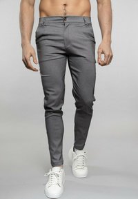Pantalons gris ajustés fabriqués à partir d'un matériau lisse, avec une fermeture à bouton à l'avant et des poches arrière. Complétés par des baskets blanches.