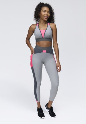 Gray activewear set featuring a sports bra and high-waisted leggings with pink accents. Smooth, stretchy fabric with a snug fit. Black athletic shoes.