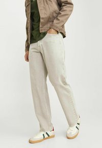 Jeans de denim gris claro con corte recto, sutiles desgastes y detalles de costura. Combinados con una camisa verde y una chaqueta marrón para crear contraste.