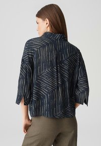 Marinebluse mit geometrischem grauem Muster, mit kurzen Ärmeln und einem lockeren Schnitt. Weiches Material mit Kragen und Rückenfalte.