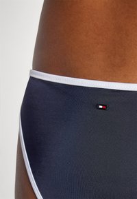 Costume da bagno navy con elastico bianco in vita e piccolo logo del marchio in rosso, bianco e nero. Texture liscia, design aderente.