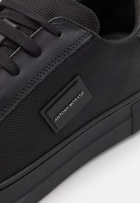 Baskets noires en maille texturée et cuir, avec des lacets plats, une semelle en caoutchouc épaisse et une étiquette noire portant "ANTONY MORATO."