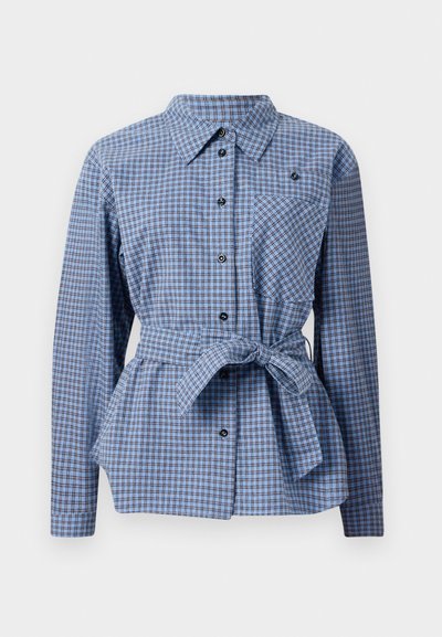 Sinine ja valge ruuduline särk nööbiga ees, pikkade varrukatega, seotud vöökohaga ja rinnataskuga. Omab musti nööpe ja teravat kraed.