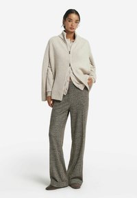 Beige stickad cardigan med hög krage och knäppning, tillsammans med grå mönstrade vida byxor. Båda plaggen har en lös passform.