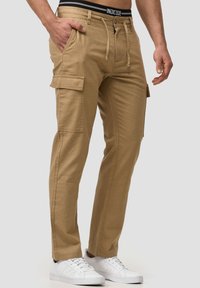 Pantalons cargo kaki en mélange de coton, avec poches latérales, fermeture à bouton et taille à cordon de serrage. Baskets blanches incluses.