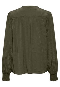 Blouse vert olive avec un motif à pois texturé, présentant un pli au dos et des poignets élastiqués. Conception légère à manches longues.