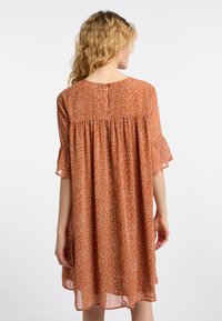 Oranje bloemenjurk met korte gerimpelde mouwen, een geraffineerde rug en een keyhole knoopsluiting bij de hals. Lichtgewicht, vloeiende stof.